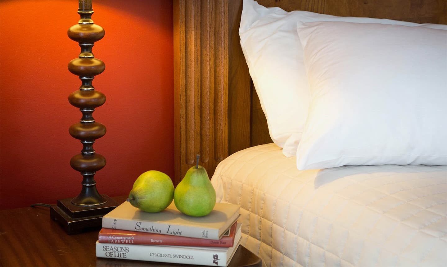 Closeup of books, two pears, lamp next to pillows in Chowan Room