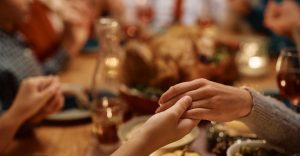 mother and daughter holding hands during family prayer on Thanksgiving at dining tabl