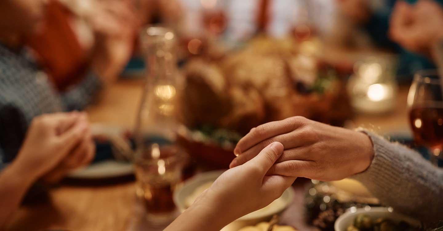 mother and daughter holding hands during family prayer on Thanksgiving at dining tabl