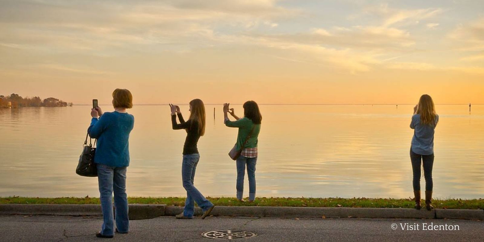 A group of two mothers and their daughters taking pictures of the sunset over the water in Edenton, NC