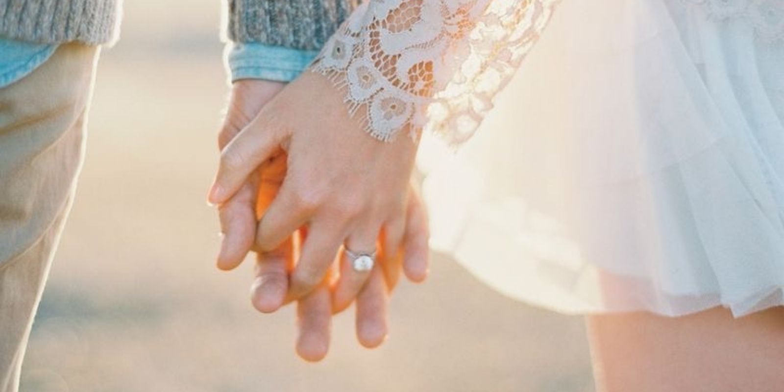 A close-up image of a couple holding hands, with the focus on the woman's hand showing an engagement ring.