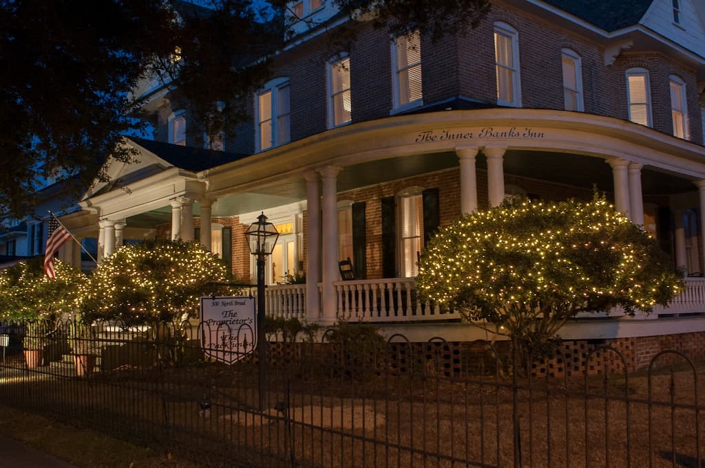 A large house illuminated at night, showcasing its front facade with warm lights glowing from the windows.