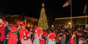 A crowd wearing Santa hats gathers around a decorated Christmas tree during the Edenton Christmas celebration.