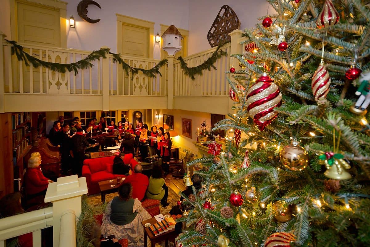 A beautifully decorated Christmas tree with ornaments, surrounded by people enjoying the festive atmosphere in a cozy room.