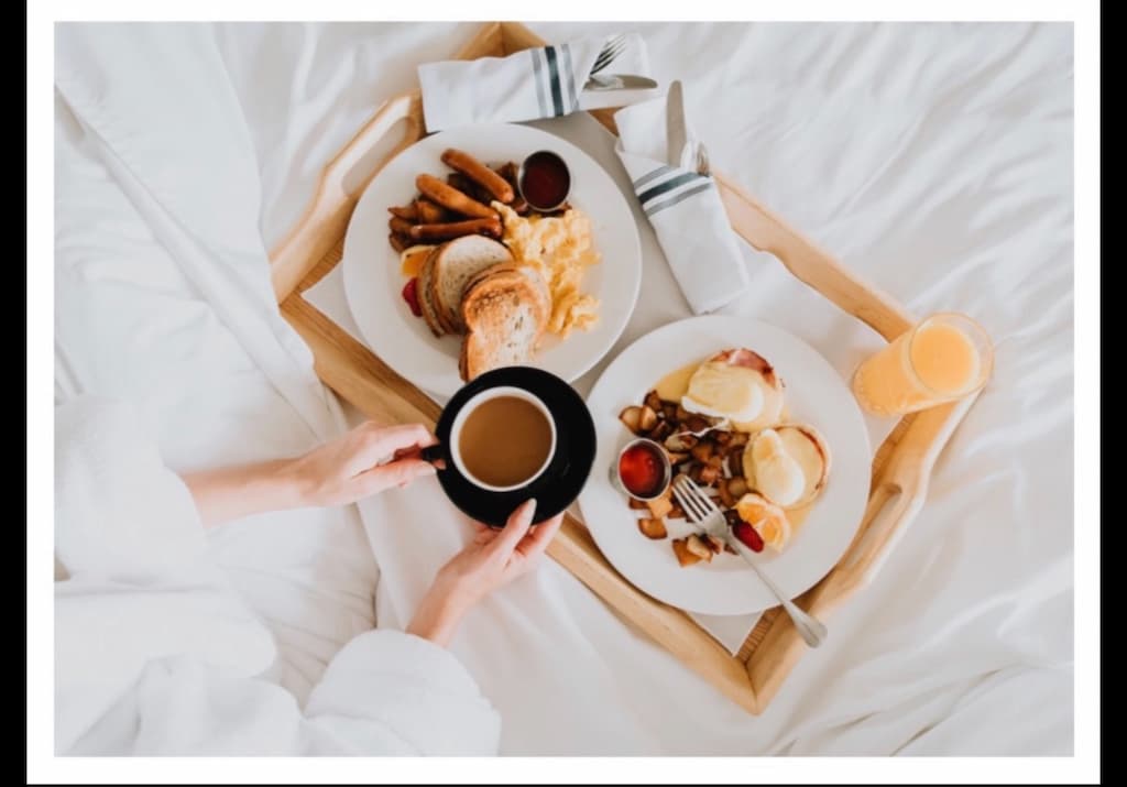A woman sitting in bed looking down at her coffee and tray of breakfast food during her babymoon getaway at our North Carolina bed and breakfast.