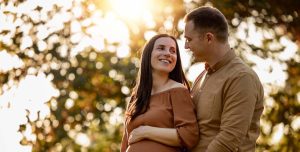 A pregnant woman standing in a park with her husband during their babymoon getaway in North Carolina.