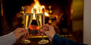 Close up of a couple's hands holding two champagne glasses by the fireplace during a romantic getaway in NC